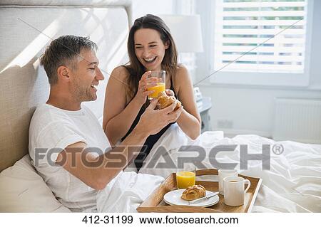 Stock Photo - Smiling couple enjoying breakfast in bed. Fotosearch