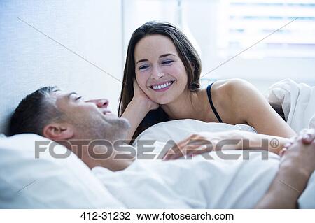 Smiling couple laying in bed talking View Large Photo Image Stock Image - Smiling couple laying in bed talking. Fotosearch