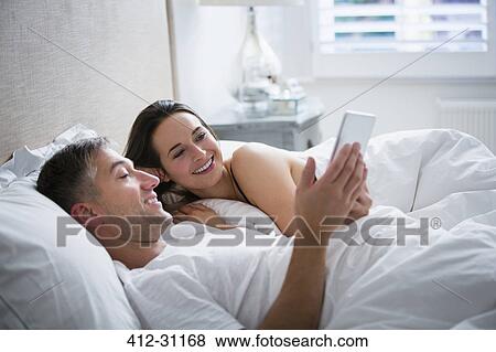 Stock Photo - Smiling couple laying in bed using digital tablet. Fotosearch