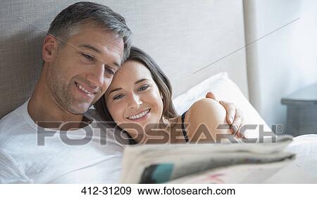 Smiling couple reading newspaper in bed View Large Photo Image Stock Photo - Smiling couple reading newspaper in bed. Fotosearch