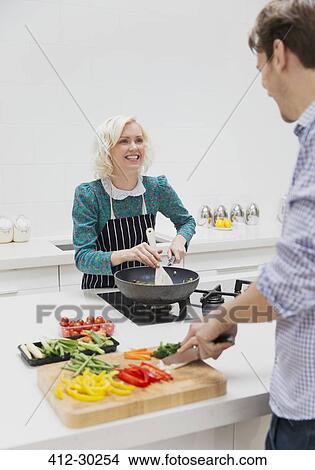 Smiling couple slicing and cooking vegetables in kitchen View Large Photo Image Picture - Smiling couple slicing and cooking vegetables in kitchen. Fotosearch