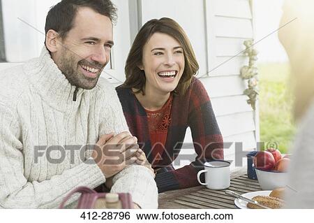Stock Photograph - Smiling couple talking at table on patio. Fotosearch