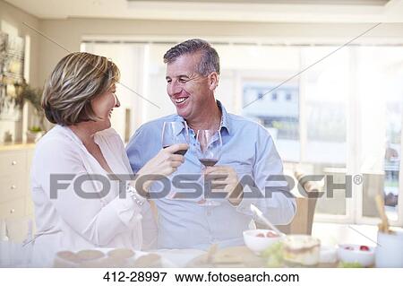 Smiling couple toasting red wine glasses in kitchen View Large Photo Image Stock Photo - Smiling couple toasting red wine glasses in kitchen. Fotosearch