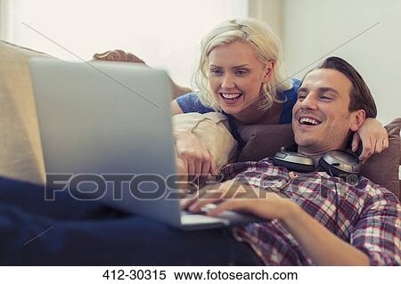 Smiling couple using laptop on living room sofa View Large Photo Image Stock Photography - Smiling couple using laptop on living room sofa. Fotosearch