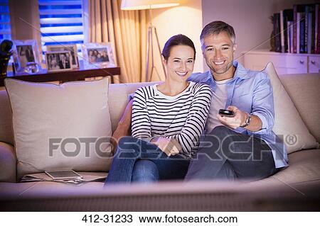 Stock Image - Smiling couple watching TV in living room. Fotosearch