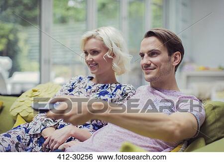 Smiling couple watching TV in living room changing channels View Large Photo Image Stock Photograph - Smiling couple watching TV in living room changing channels. Fotosearch