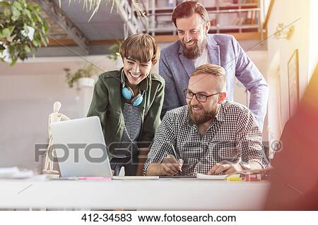 Stock Image - Smiling design professionals using graphics tablet at laptop in office. Fotosearch