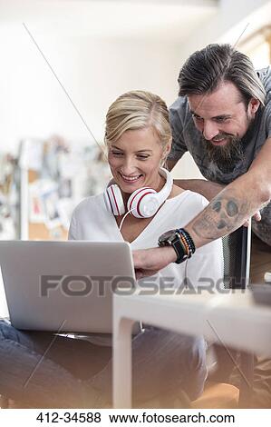 Stock Photo - Smiling design professionals working at laptop in office. Fotosearch