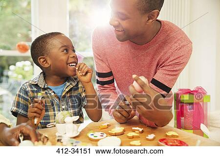 Stock Image - Smiling father and son decorating Easter eggs and cookies. Fotosearch