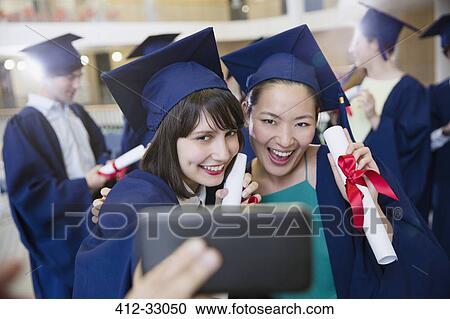 Smiling female college graduates in cap and gown taking selfie View Large Photo Image Stock Image - Smiling female college graduates in cap and gown taking selfie. Fotosearch