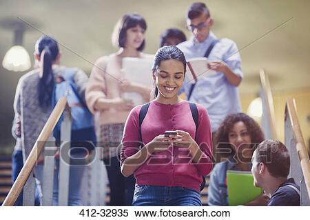 Stock Photography - Smiling female college student texting in stairway. Fotosearch