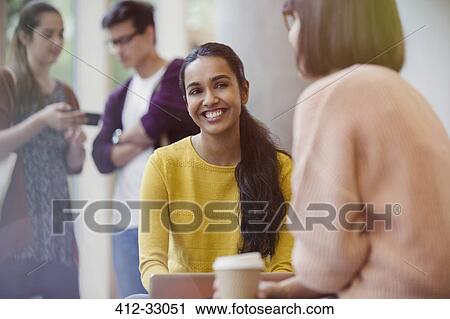 Stock Image - Smiling female college students drinking coffee and talking. Fotosearch
