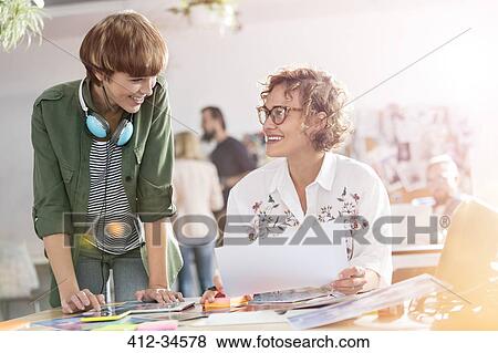 Smiling female design professionals reviewing proofs in office View Large Photo Image Stock Photo - Smiling female design professionals reviewing proofs in office. Fotosearch