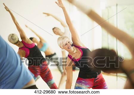 Stock Image - Smiling fitness instructor leading aerobics class stretching arms. Fotosearch