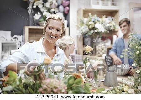 Stock Image - Smiling florist arranging bouquet in flower shop. Fotosearch