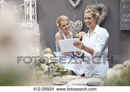 Picture - Smiling florists using digital tablet in flower shop. Fotosearch