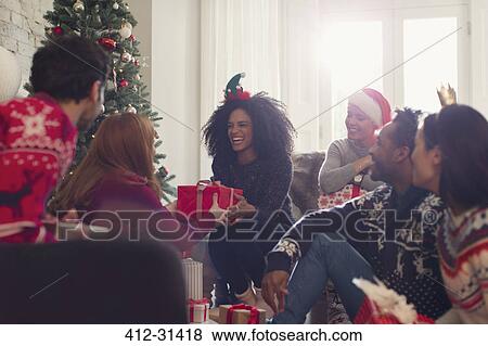Stock Photo - Smiling friends exchanging Christmas gifts in living room. Fotosearch