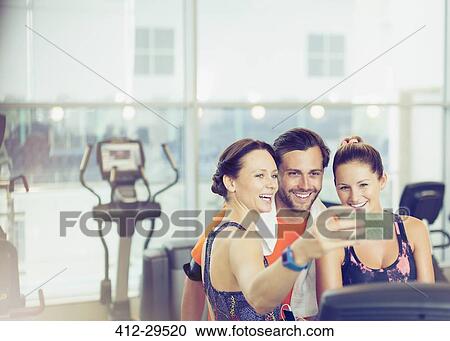 Stock Image - Smiling friends taking selfie at gym. Fotosearch