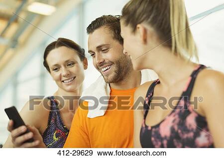 Smiling friends using cell phone at gym View Large Photo Image Stock Photo - Smiling friends using cell phone at gym. Fotosearch