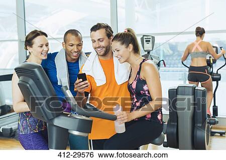 Smiling friends using cell phone at exercise bike in gym View Large Photo Image Stock Photograph - Smiling friends using cell phone at exercise bike in gym. Fotosearch