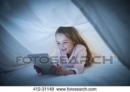 Smiling girl using digital tablet under sheet View Large Photo Image Stock Photo - Smiling girl using digital tablet under sheet. Fotosearch