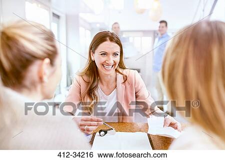 Stock Photograph - Smiling jeweler showing diamond to women in jewelry store. Fotosearch