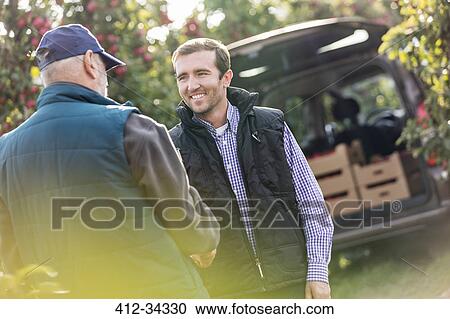 Smiling male farmer and customer handshaking in apple orchard View Large Photo Image Stock Image - Smiling male farmer and customer handshaking in apple orchard. Fotosearch