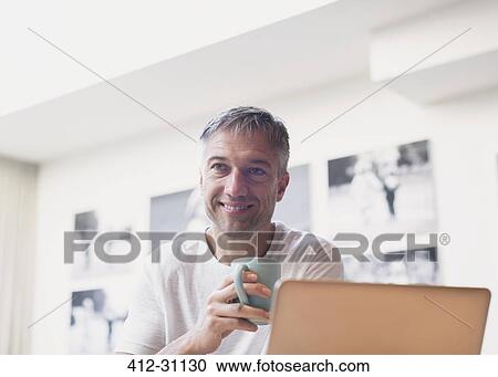 Smiling man drinking coffee at laptop View Large Photo Image Stock Image - Smiling man drinking coffee at laptop. Fotosearch