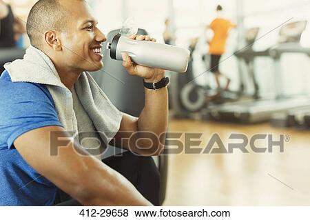 Smiling man drinking water at gym View Large Photo Image Stock Photo - Smiling man drinking water at gym. Fotosearch