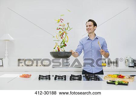 Smiling man flipping vegetables in skillet in kitchen View Large Photo Image Stock Photo - Smiling man flipping vegetables in skillet in kitchen. Fotosearch
