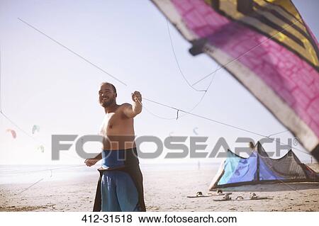 Smiling man pulling kiteboarding kite on sunny beach View Large Photo Image Stock Photo - Smiling man pulling kiteboarding kite on sunny beach. Fotosearch
