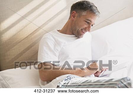 Smiling man using digital tablet in bed View Large Photo Image Stock Photo - Smiling man using digital tablet in bed. Fotosearch