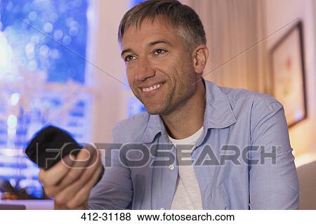 Stock Photo - Smiling man with remote control watching TV. Fotosearch