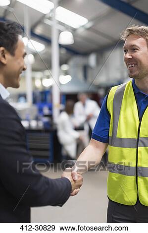 Stock Photo - Smiling manager and worker handshaking in steel factory. Fotosearch
