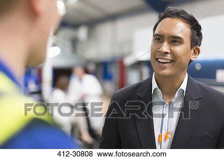 Stock Photo - Smiling manager talking with worker in steel factory. Fotosearch