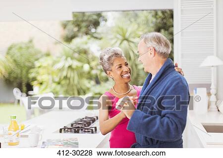 Stock Photo - Smiling mature couple dancing in kitchen. Fotosearch