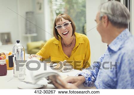 Stock Photo - Smiling mature couple reading newspaper at breakfast table. Fotosearch