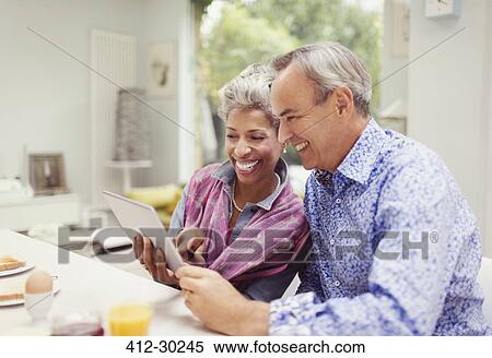 Smiling mature couple sharing digital tablet at breakfast table View Large Photo Image Stock Photography - Smiling mature couple sharing digital tablet at breakfast table. Fotosearch