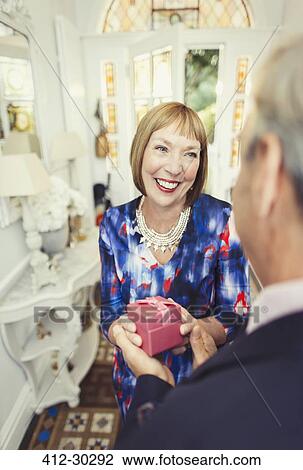 Stock Image - Smiling mature woman receiving gift from husband. Fotosearch