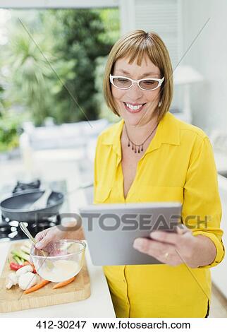 Smiling mature woman using digital tablet and cooking in kitchen View Large Photo Image Stock Photo - Smiling mature woman using digital tablet and cooking in kitchen. Fotosearch
