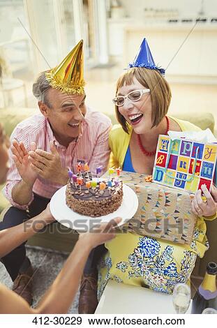 Stock Photo - Smiling mature women receiving birthday cake and gifts. Fotosearch