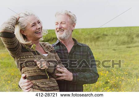 Stock Image - Smiling senior couple hugging in field. Fotosearch