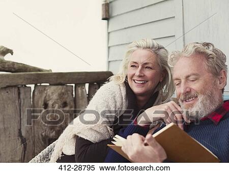 Stock Photography - Smiling senior couple reading book on patio. Fotosearch