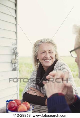 Stock Image - Smiling senior couple talking at patio table. Fotosearch