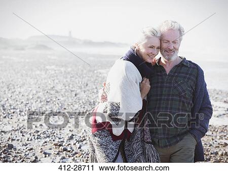 Stock Image - Smiling senior couple walking on beach. Fotosearch