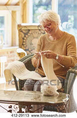 Stock Image - Smiling senior woman knitting scarf. Fotosearch