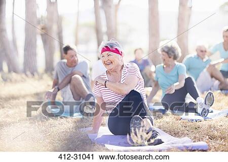 Stock Image - Smiling senior woman practicing yoga in sunny park. Fotosearch