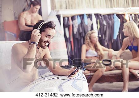 Smiling surfer listening to music with headphones and mp3 player View Large Photo Image Stock Image - Smiling surfer listening to music with headphones and mp3 player. Fotosearch