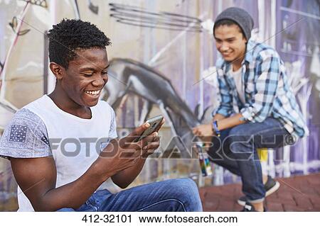 Smiling teenage boys hanging out texting and spray painting graffiti on urban wall View Large Photo Image Stock Image - Smiling teenage boys hanging out texting and spray painting graffiti on urban wall. Fotosearch
