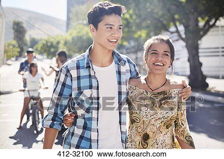 Smiling teenage couple walking on sunny urban street View Large Photo Image Stock Image - Smiling teenage couple walking on sunny urban street. Fotosearch